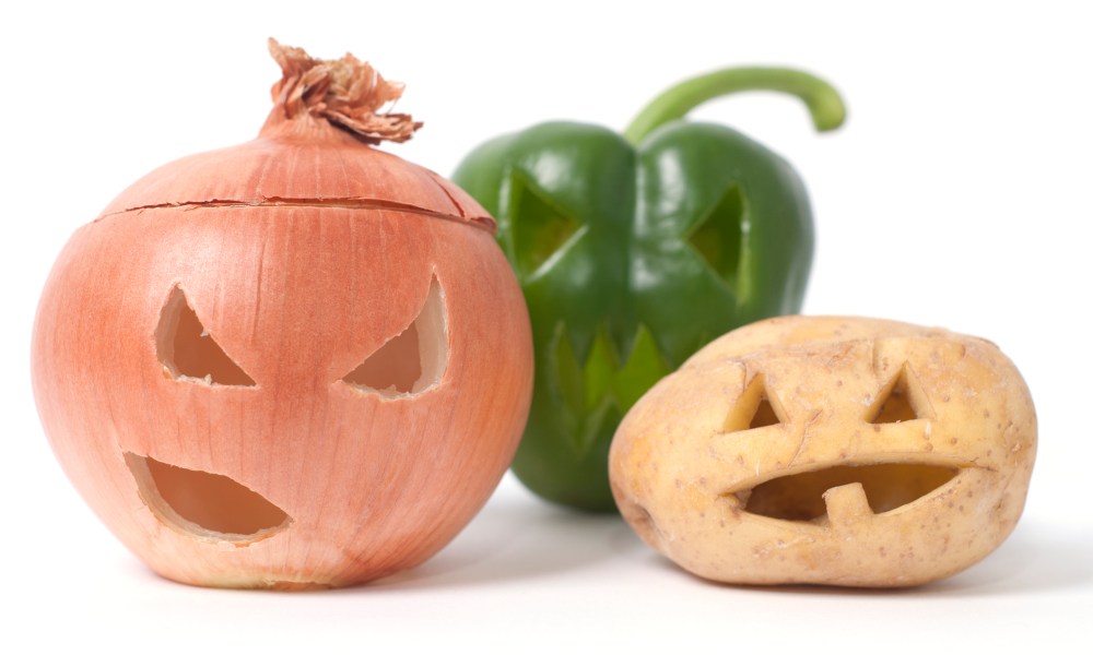 An onion, a bell pepper, and a potato all carved into jack-o-lanterns on a white background