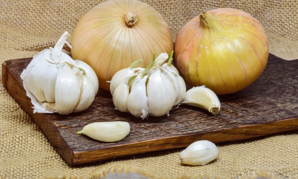 Garlic bulbs and cloves and two onions on a wooden cutting board